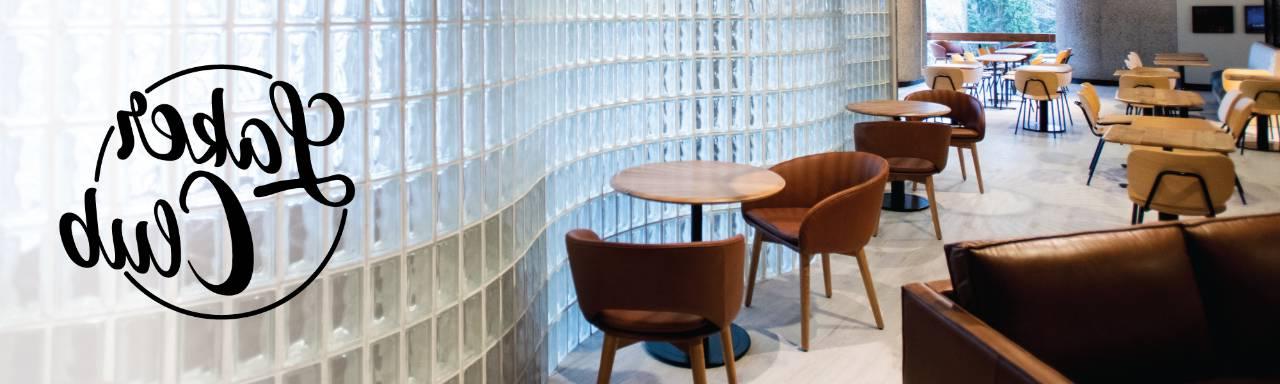 Interior of Laker Club, a curved glass brick wall next to brown chairs and tables